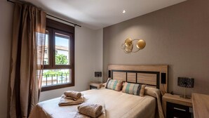 A bedroom with a large bed, two bedside tables, a wall-mounted lamp, and a window with curtains.