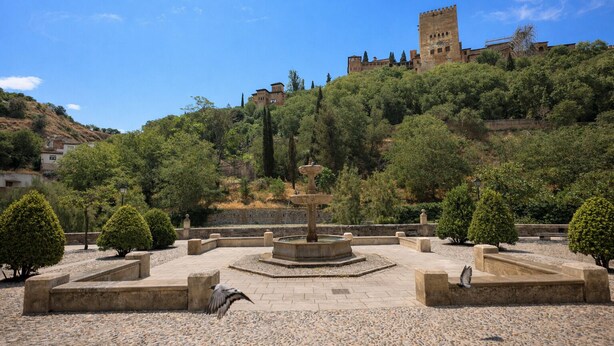 A courtyard with a fountain, stone benches, and a castle in the background.