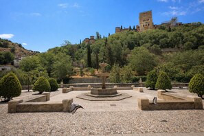 Une cour avec une fontaine, des bancs en pierre et un château en arrière-plan.