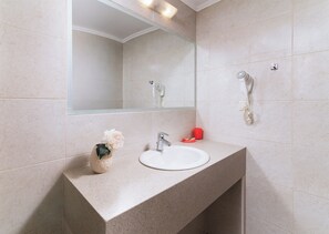A bathroom with a large mirror, a sink, and a hairdryer mounted on the wall. - Eva Marina Hotel (Faistos)