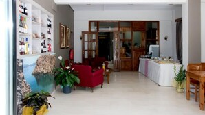 A spacious living area with a red sofa, a dining table set for a meal, and a large window overlooking a scenic view. - Eva Marina Hotel (Faistos)