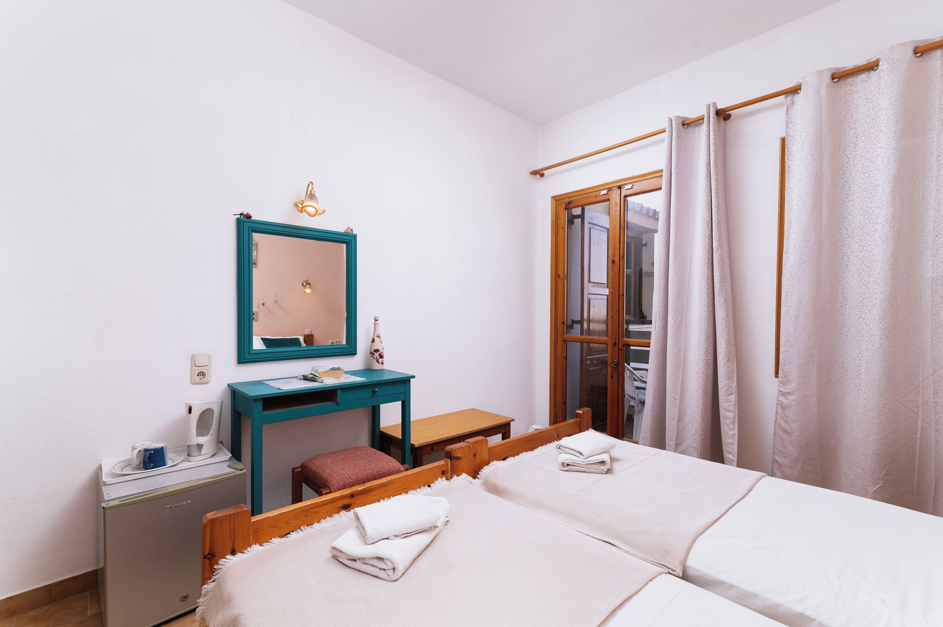 A bedroom with two beds, a wooden desk, a mirror, and a window with curtains.