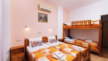 A bedroom with two single beds, a bunk bed, wooden furniture, an air conditioner, and a painting on the wall.