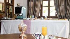 A breakfast table with a coffee machine, a jug, a glass of orange juice, a teapot, and a plate with toast and a donut. - Eva Marina Hotel (Faistos)