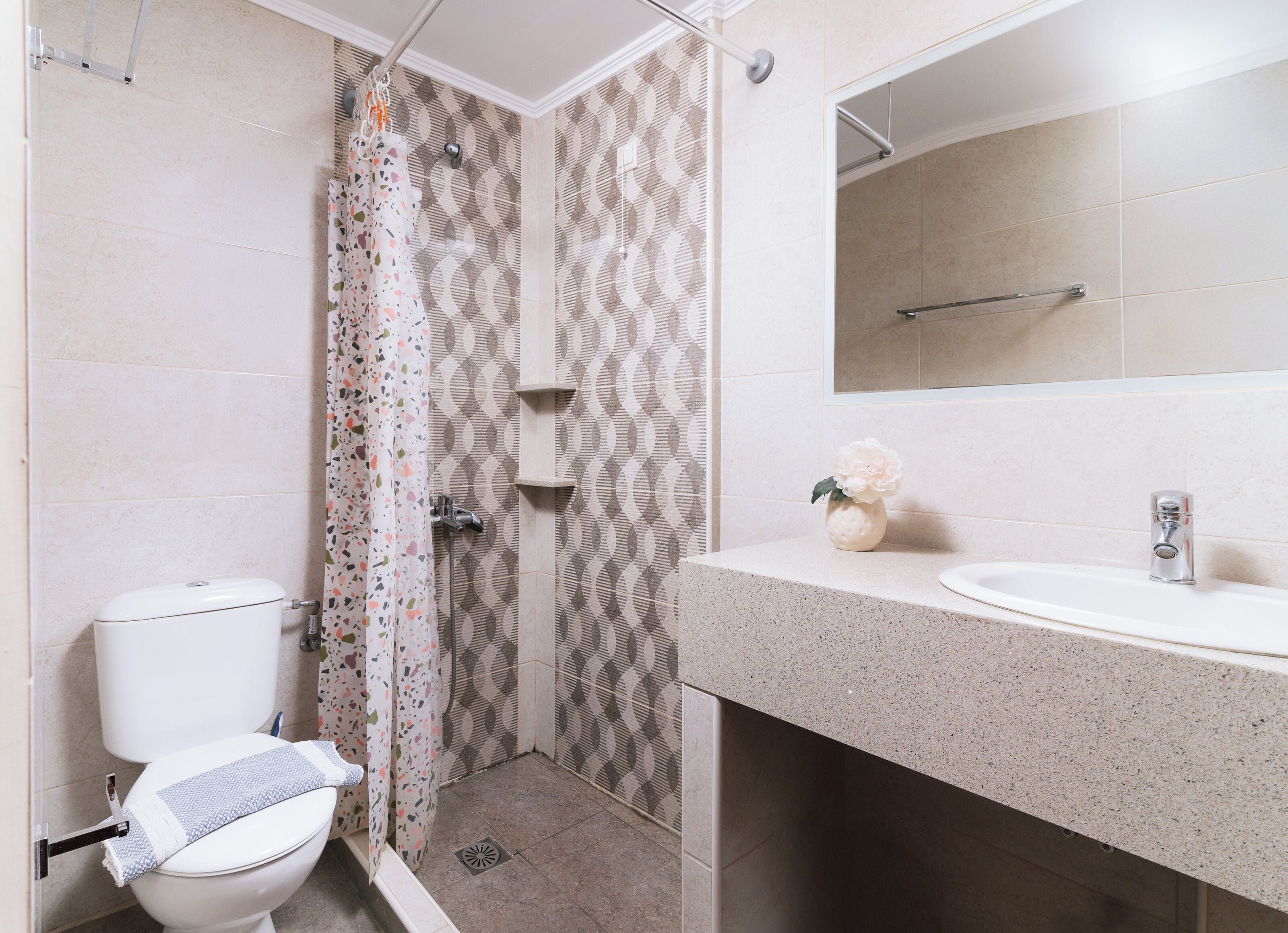 A bathroom with a shower, toilet, sink, and mirror.
