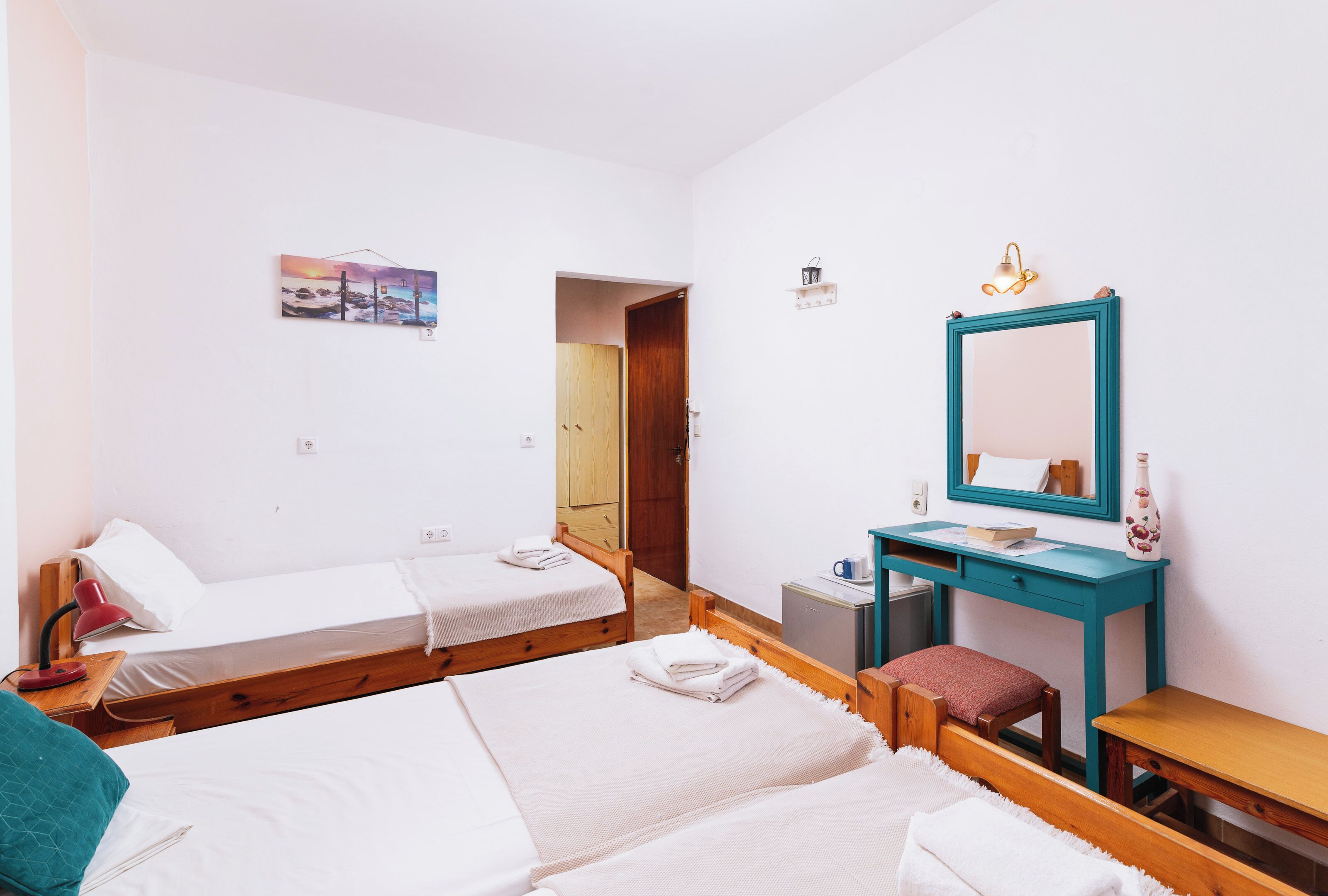 Una habitación con dos camas individuales, un escritorio de madera, un espejo y un armario pequeño.