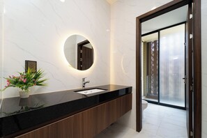 A modern bathroom with a black countertop, a round mirror, and a wooden cabinet. - The Global City - Jenny Residences (Ho Chi Minh City)