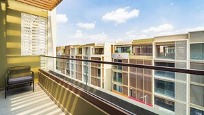 A balcony with a chair, a view of modern buildings, and a sign indicating a public space. - The Global City - Jenny Residences (Ho Chi Minh City)
