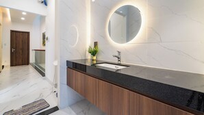 A modern bathroom with a marble floor, a black countertop, and a round mirror. - The Global City - Jenny Residences (Ho Chi Minh City)