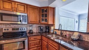A kitchen with wooden cabinets, stainless steel appliances, a granite countertop, and a window with blinds.