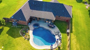 Vista aérea de una casa con piscina, muebles de patio y jardín cercado.