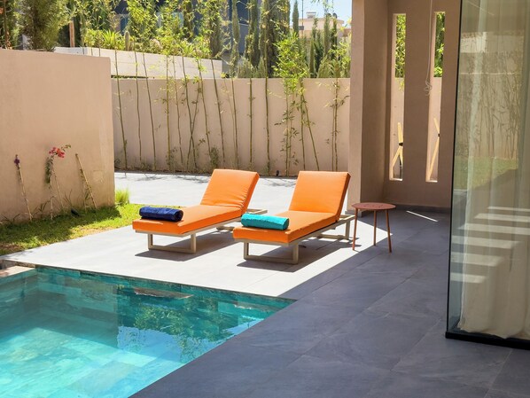 A poolside area with two orange lounge chairs, a small round table, and a glass-enclosed space.
