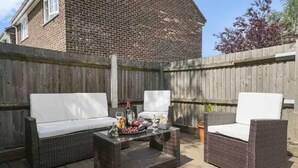 An outdoor patio with wicker furniture, a coffee table, and a brick wall in the background. - 5 Bed House - Sleeps 10 - Garden - Parking - Wifi (Aylesford)