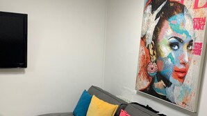 A grey sofa with colorful cushions, a flat-screen TV, and a vibrant magazine cover on the wall. - 5 Bed House - Sleeps 10 - Garden - Parking - Wifi (Aylesford)