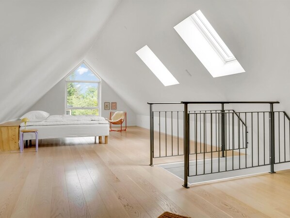 A spacious attic bedroom with a large window, a bed, a chair, and a black metal gate.