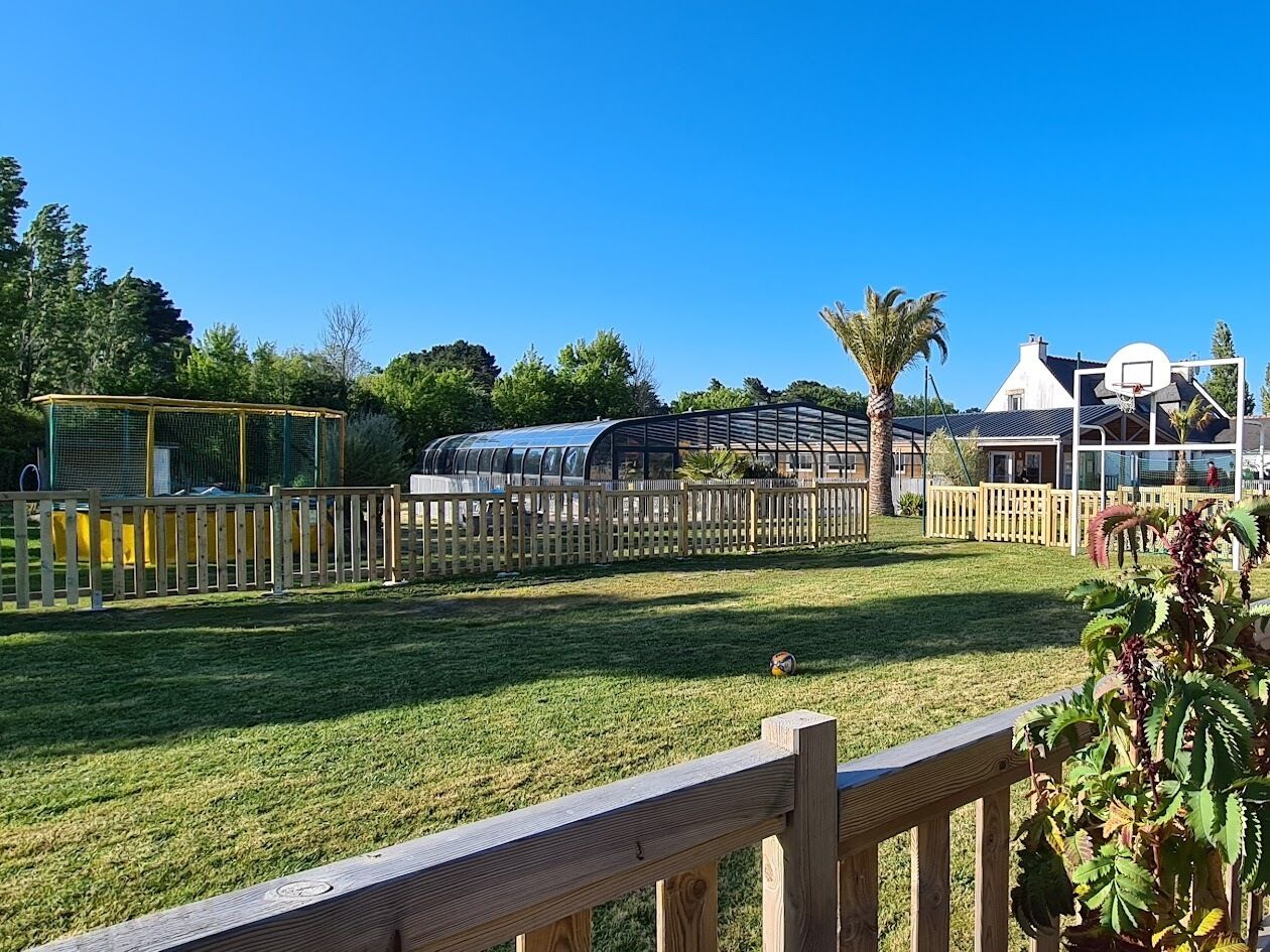 A fenced outdoor area with a greenhouse, a basketball hoop, and a house in the background.
