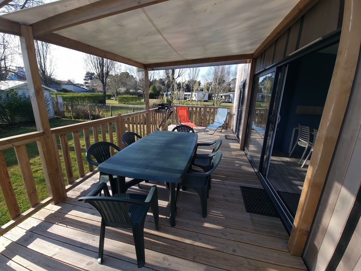 Una terraza techada al aire libre con una mesa y sillas, baranda de madera y vistas del paisaje circundante.