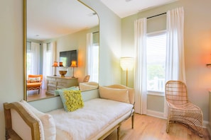 A bedroom with a bed, a chair, a dresser, a mirror, and a window with curtains.