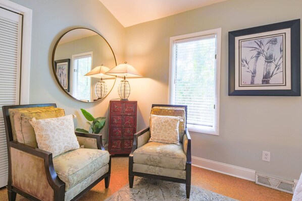 A room with two armchairs, a mirror, a lamp, a red cabinet, and a framed picture on the wall.