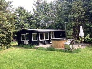 A log cabin with a deck, surrounded by a grassy yard and dense trees. - 6 Person Holiday Home in Idestrup (Idestrup)
