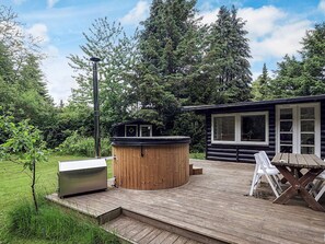 A wooden deck with a hot tub, a barbecue grill, and a dining table with chairs. - 6 Person Holiday Home in Idestrup (Idestrup)
