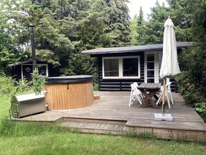A wooden deck with a hot tub, a barbecue grill, and a table with chairs. - 6 Person Holiday Home in Idestrup (Idestrup)