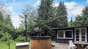 A wooden deck with a hot tub, a wooden cabin, and a table with chairs.