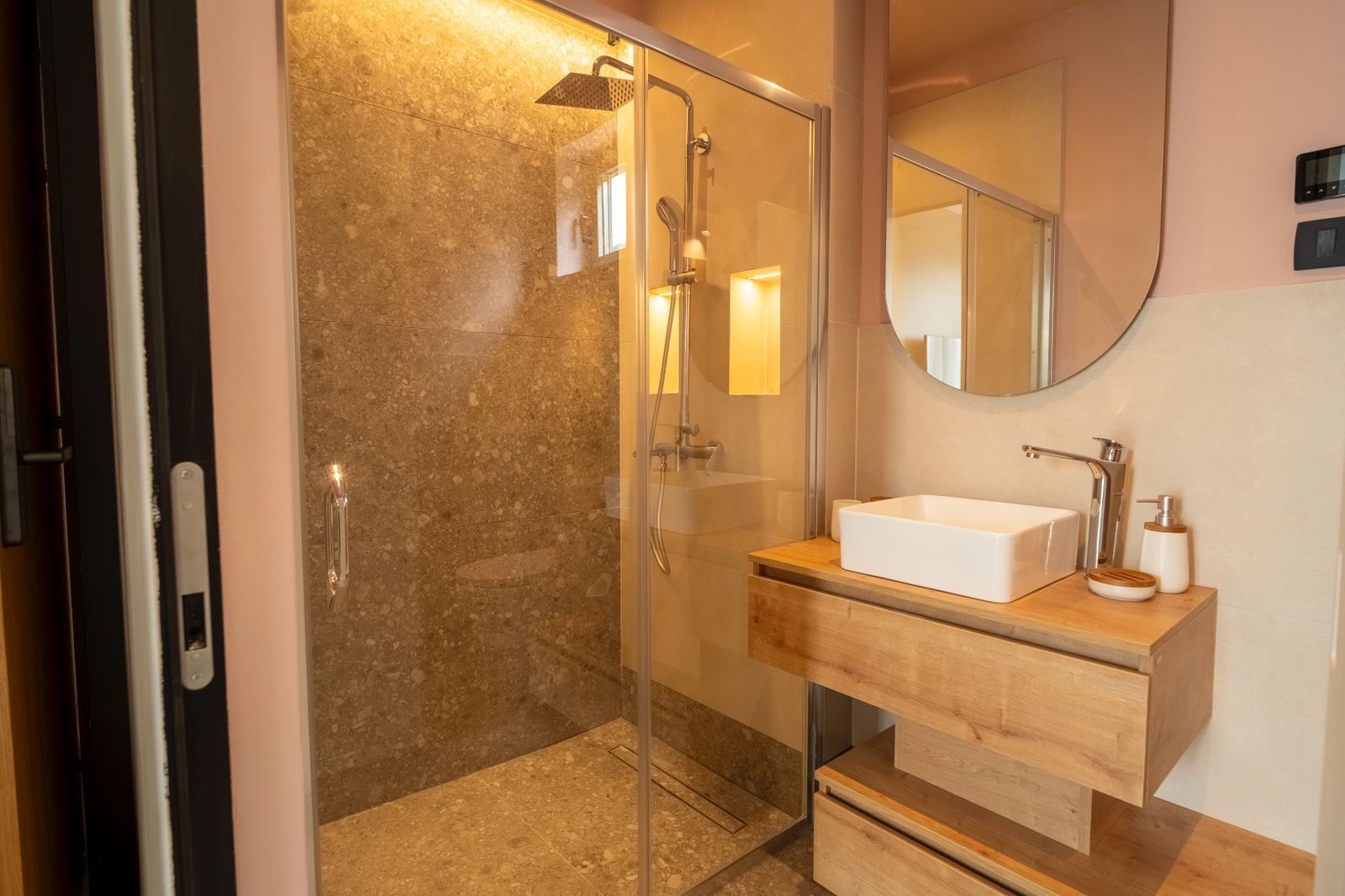 Un baño moderno con ducha de vidrio, tocador de madera y espejo redondo.
