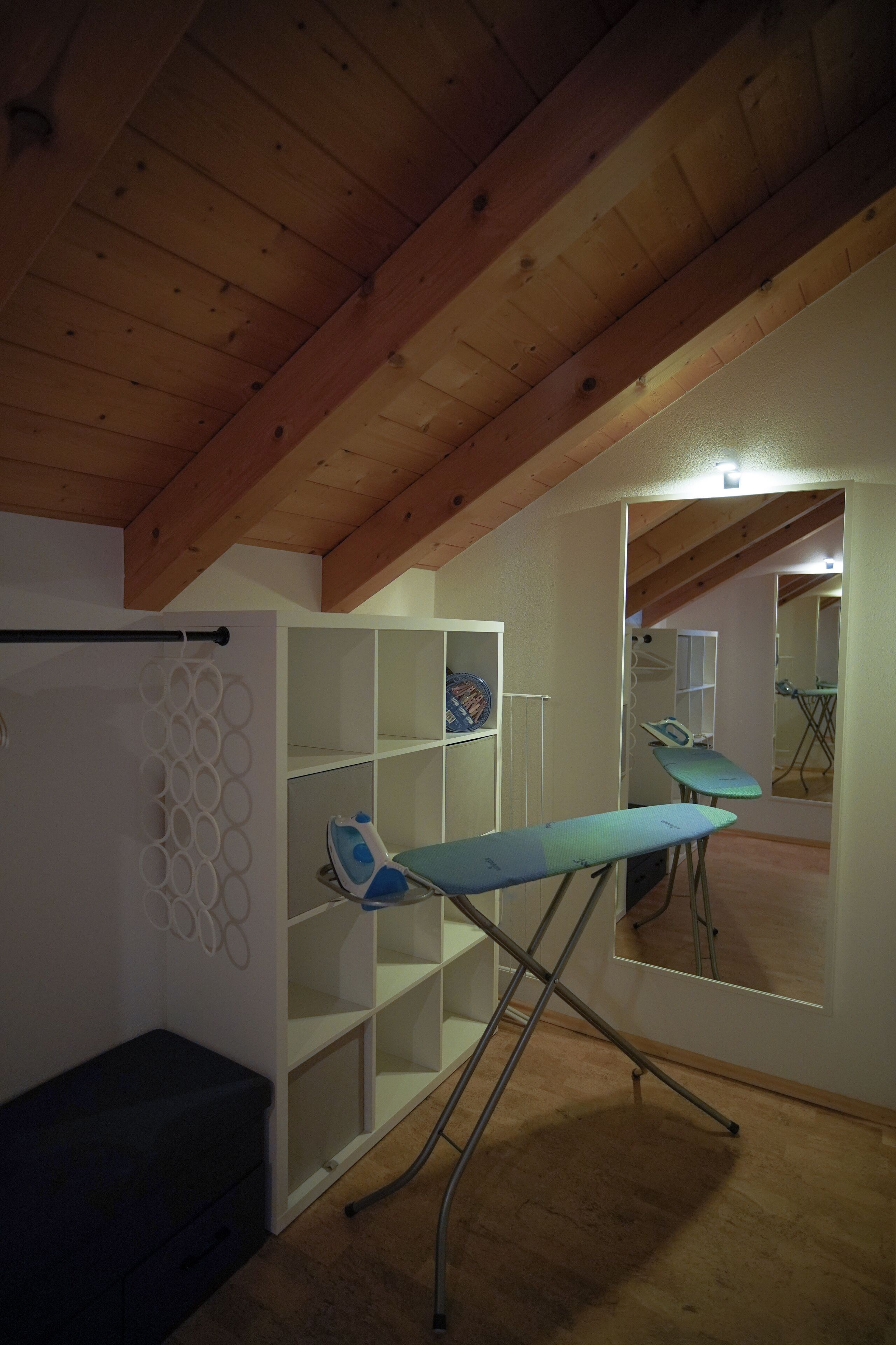 Ein Zimmer mit schrägem Dach, einem Bügelbrett und einer Spiegelwand.