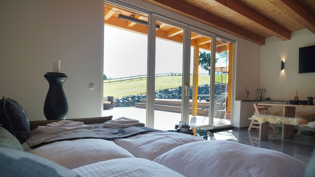A bedroom with a large bed, a vase, and a view of a patio with a table and chairs. - Alpen Lodges Gindels - Space for 10 - (Rettenberg)