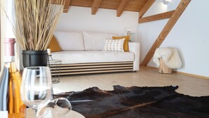 A cozy loft bedroom with a sloped ceiling, a white sofa, a wooden coffee table, and a cowhide rug. - Alpen Lodges Gindels - Space for 10 - (Rettenberg)