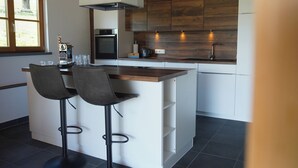A modern kitchen with a central island, bar stools, and a large window. - Alpen Lodges Gindels - Space for 10 - (Rettenberg)