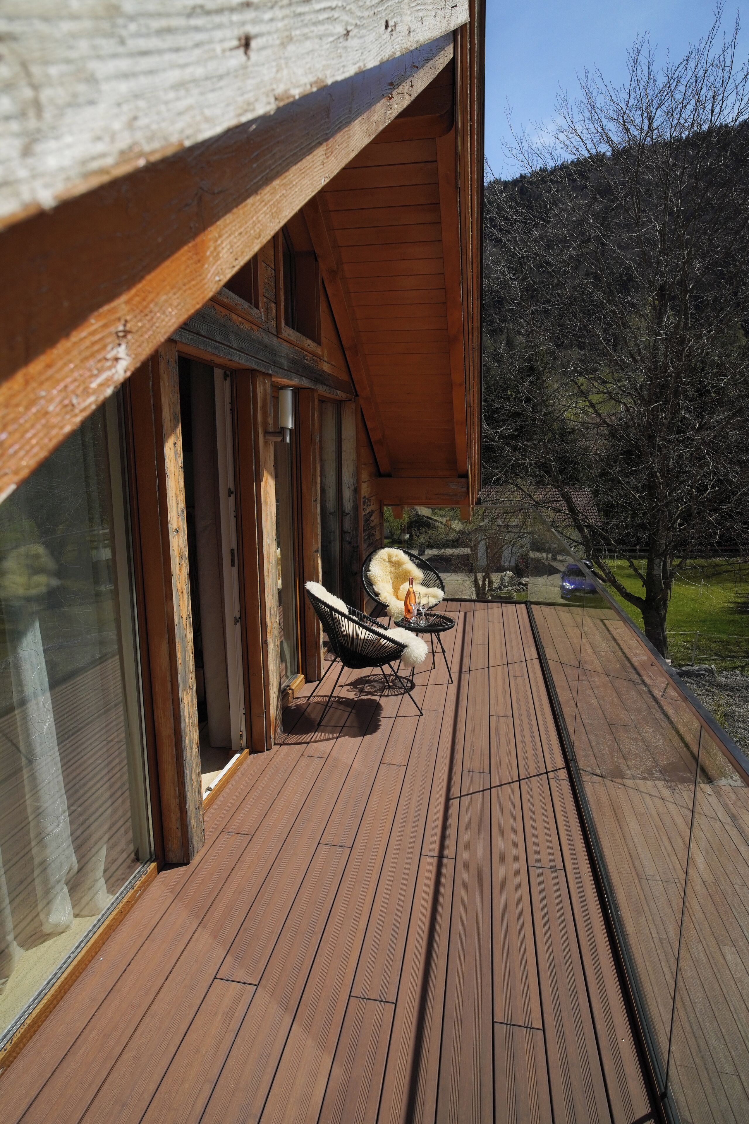 Una terraza de madera con una silla y una mesa, con vista a un área verde y árboles.