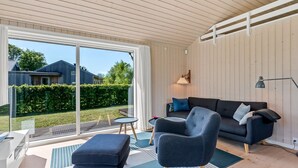 A modern living room with a sofa, armchair, and ottoman, a small table, and a large sliding glass door leading to a garden. - "Kody" - 400m from the sea by Interhome (Ebeltoft)