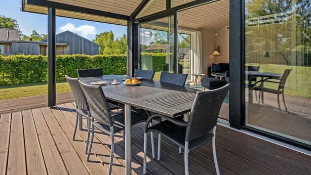 A covered outdoor dining area with a table and chairs, large windows, and a view of the backyard. - "Kody" - 400m from the sea by Interhome (Ebeltoft)