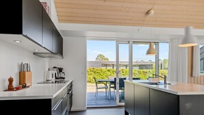 A modern kitchen with a large island, a dining area with a table and chairs, and a view of a garden through glass doors. - "Kody" - 400m from the sea by Interhome (Ebeltoft)