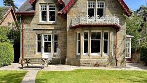 Una casa in pietra con tetto rosso, un balcone con ringhiere bianche e un vialetto lastricato che conduce all'ingresso.