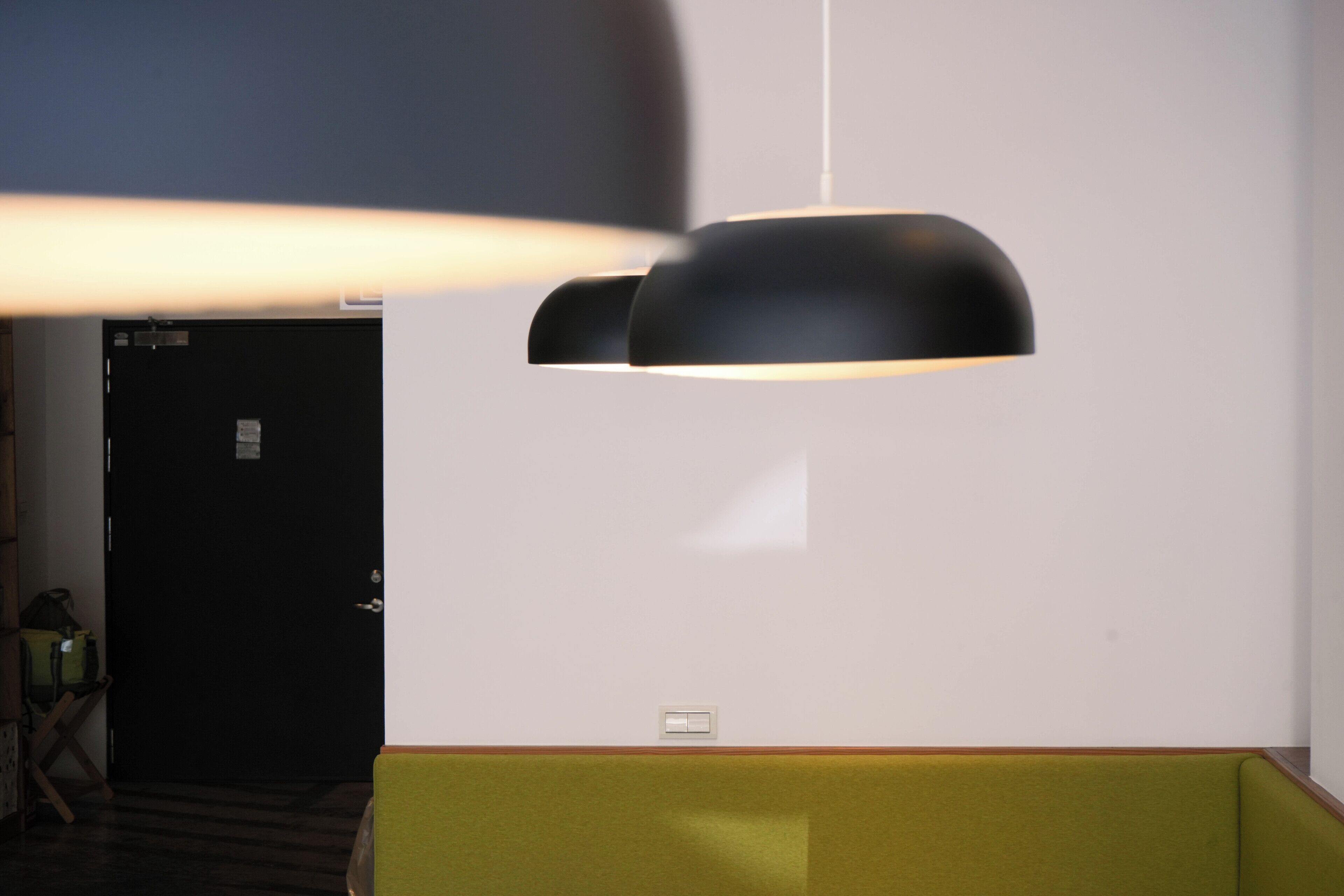 A room with a green cushioned bench, a black pendant light, and a door in the background.