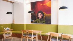 A restaurant interior with green booths, wooden tables, and chairs. There are black pendant lights and a large painting on the wall. - Yǒu mǒu hostel (Tainan)