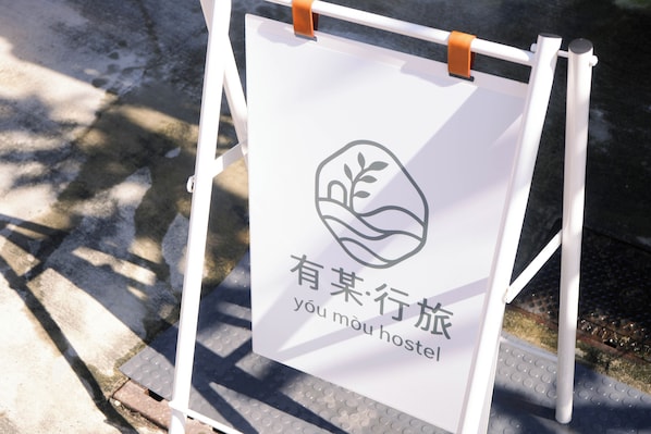 A sign with a logo and text, mounted on a white stand with brown straps.