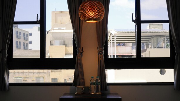 A room with a large window, a table with a lamp, and a view of buildings outside. - Yǒu mǒu hostel (Tainan)