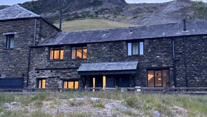 Un edificio de piedra con varias ventanas y techo plano, frente a un paisaje montañoso.