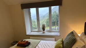 Un dormitorio con un ventanal grande, una cama con ropa de cama blanca y vistas a un paisaje montañoso.