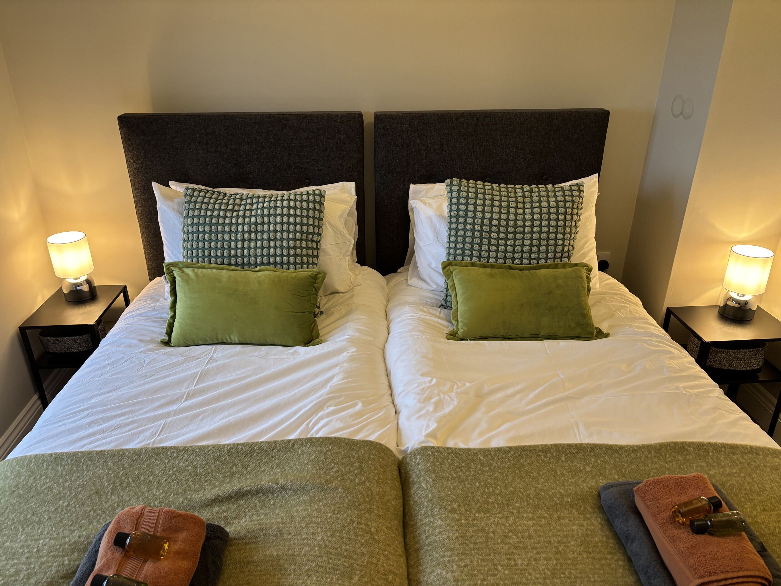 A double bed with two nightstands, each with a lamp, and green and white bedding.