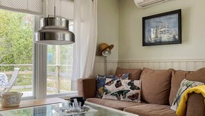 A cozy living room with a glass-top coffee table, a brown sofa with patterned cushions, a framed picture on the wall, and a window with curtains. - 4 Star Holiday Home in Norrtalje (Norrtälje)