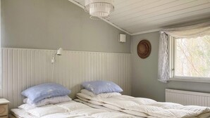 A room with a bed, a bedside table, a lamp, a radiator, and a window with a curtain. - 4 Star Holiday Home in Norrtalje (Norrtälje)