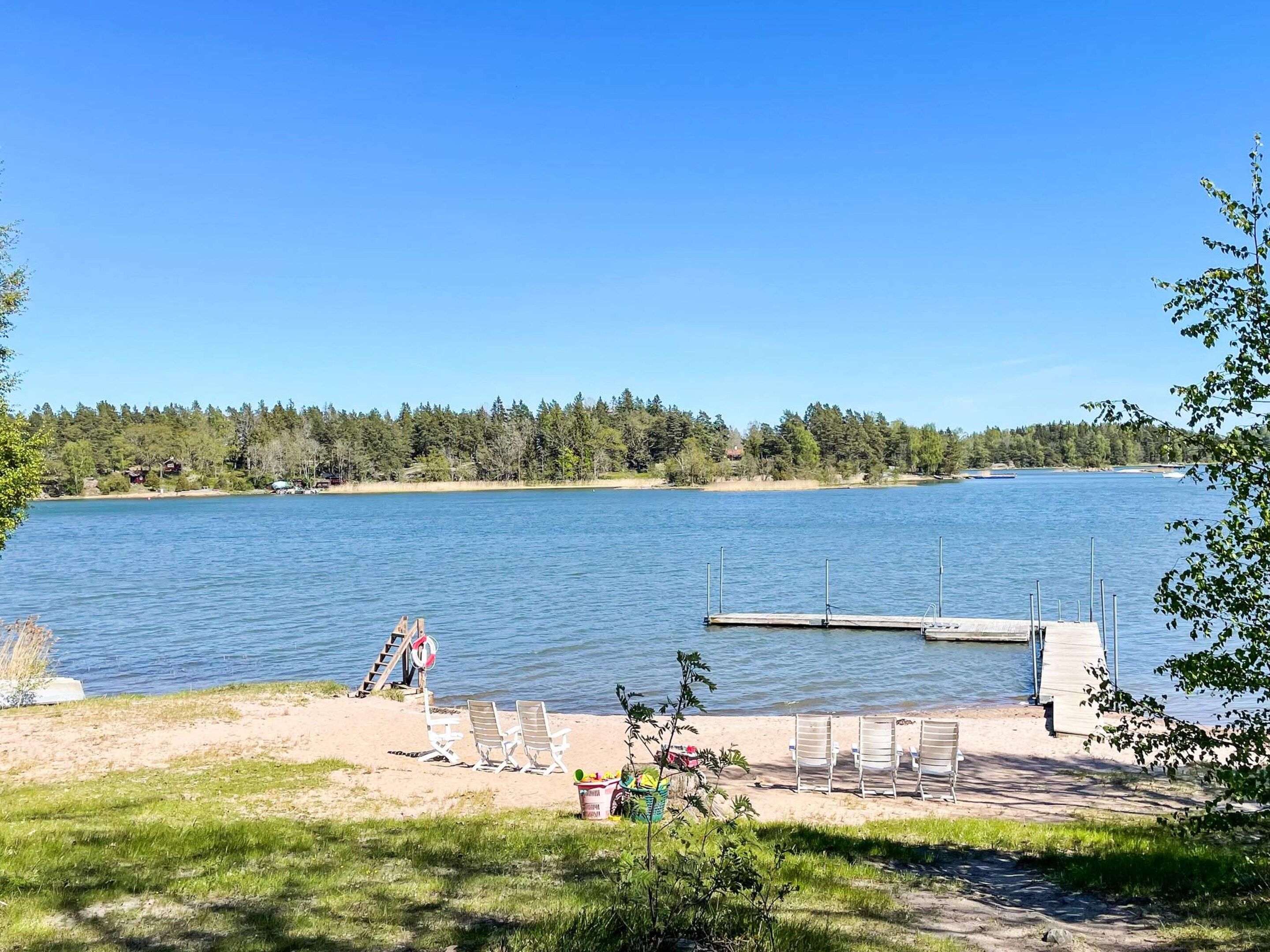 Vista de un lago con un muelle, sillas de playa y un bote pequeño.