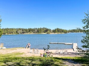 Vista de un lago con un muelle, sillas de playa y un bote pequeño.