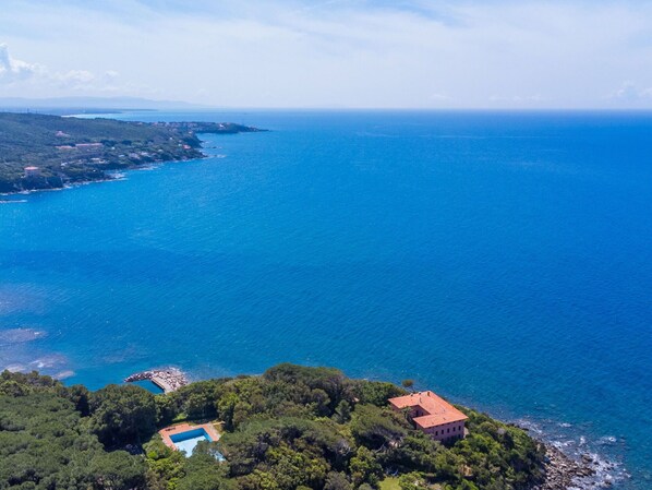 A coastal property with a swimming pool, a red-roofed building, and lush greenery.