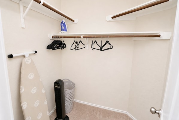 A bathroom with a towel rack, an ironing board, a hairdryer, and a laundry basket.